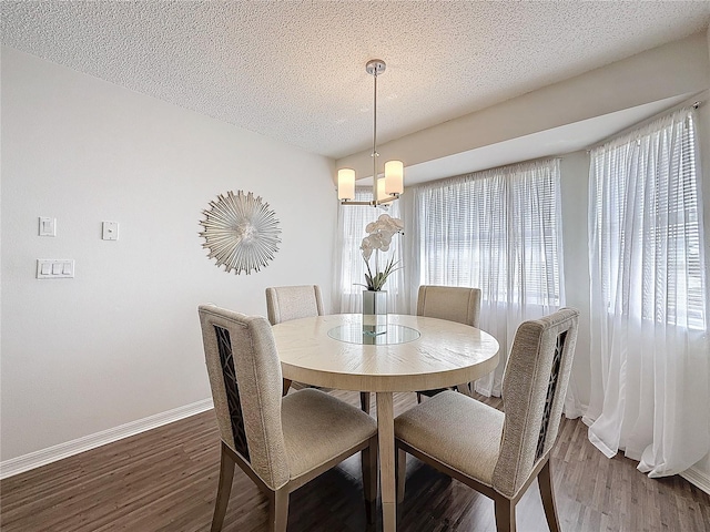 dining space with an inviting chandelier, a textured ceiling, baseboards, and wood finished floors