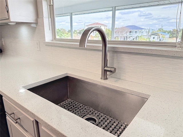 room details featuring backsplash, a sink, a residential view, and light stone countertops