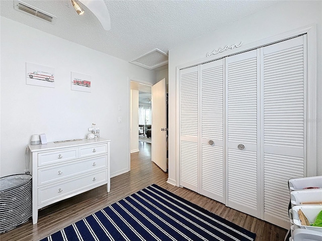 bedroom featuring a closet, visible vents, dark wood-type flooring, attic access, and a textured ceiling