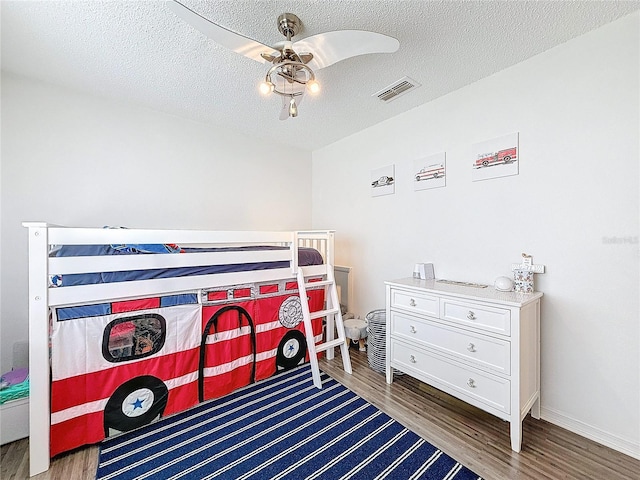 bedroom with a ceiling fan, dark wood-style flooring, visible vents, and a textured ceiling