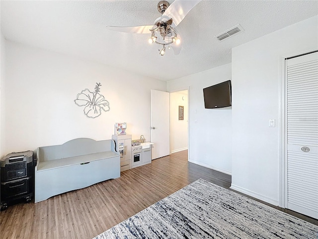 bedroom with ceiling fan, a textured ceiling, visible vents, and wood finished floors