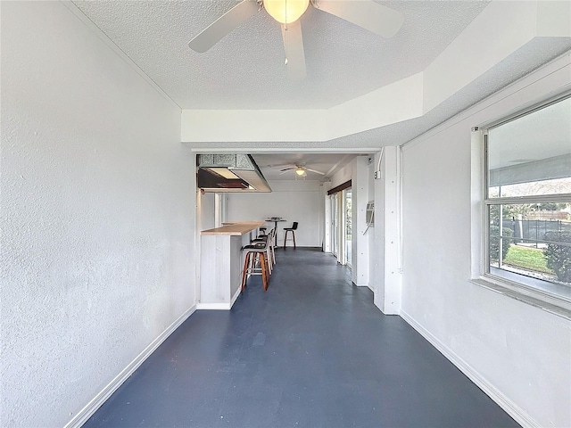 corridor with finished concrete flooring, baseboards, a textured ceiling, and a textured wall