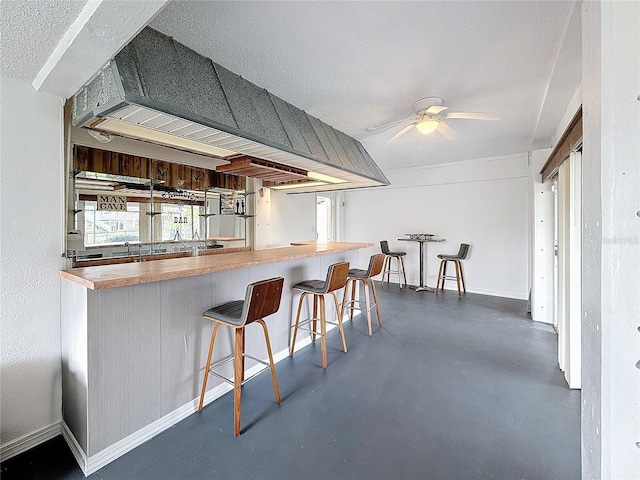 kitchen with finished concrete flooring, ceiling fan, a breakfast bar area, and baseboards