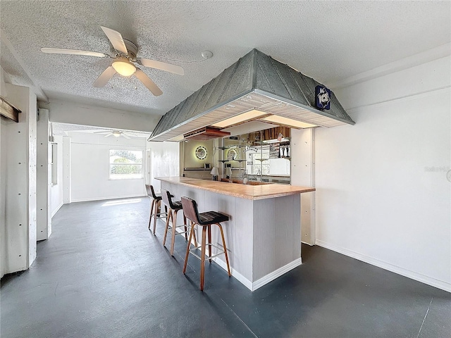 kitchen featuring a textured ceiling, a peninsula, a kitchen bar, and baseboards