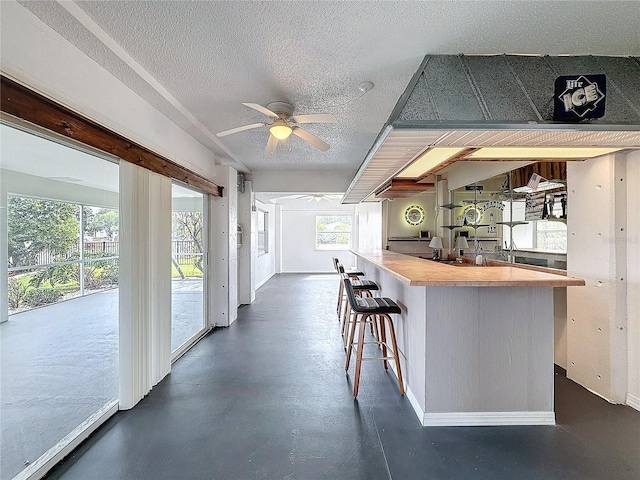 kitchen featuring ceiling fan, a breakfast bar area, concrete flooring, and a textured ceiling