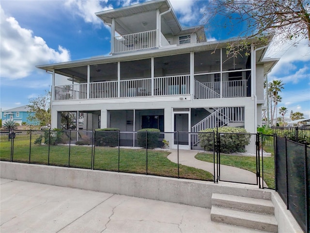 view of front of property with a fenced front yard, a balcony, a sunroom, a gate, and a front lawn