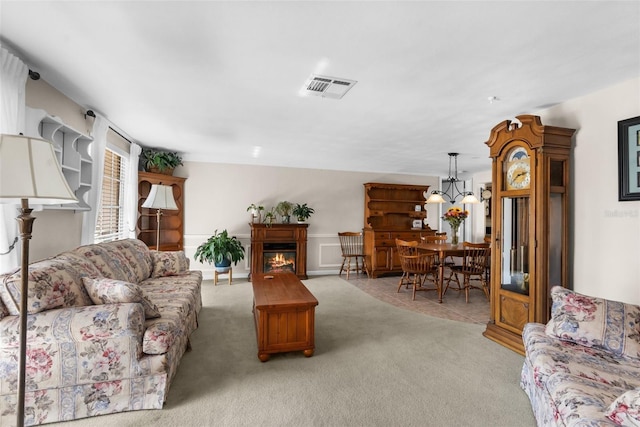 living room featuring a warm lit fireplace, light carpet, a chandelier, and visible vents