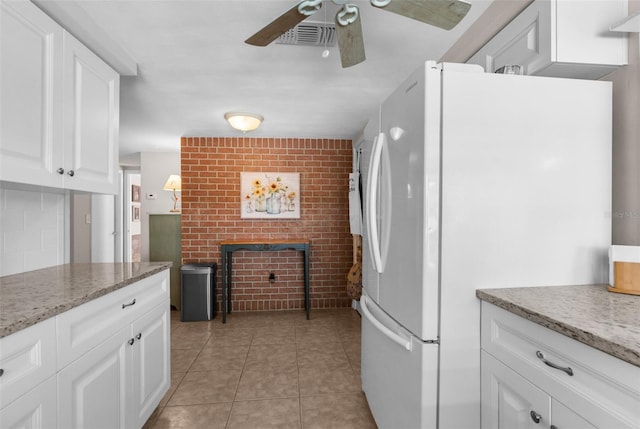 kitchen featuring brick wall, light stone counters, freestanding refrigerator, and white cabinets