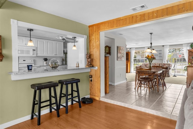 kitchen featuring white appliances, visible vents, white cabinets, a breakfast bar area, and pendant lighting