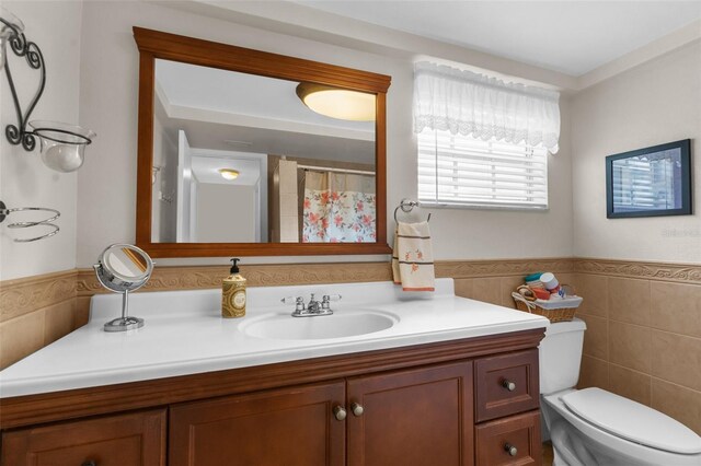 full bath with toilet, a wainscoted wall, a shower with shower curtain, vanity, and tile walls