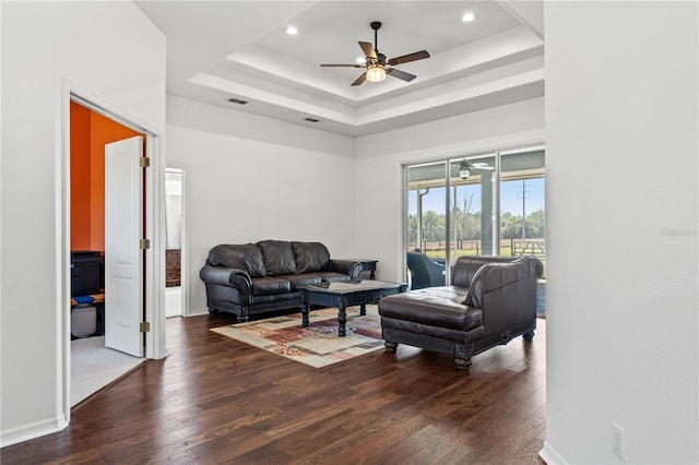 living area featuring a tray ceiling, dark wood-style floors, baseboards, and ceiling fan