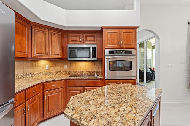 kitchen with decorative backsplash, light stone countertops, arched walkways, and stainless steel appliances