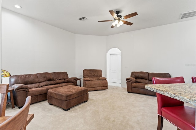 living area featuring arched walkways, a ceiling fan, visible vents, and light carpet