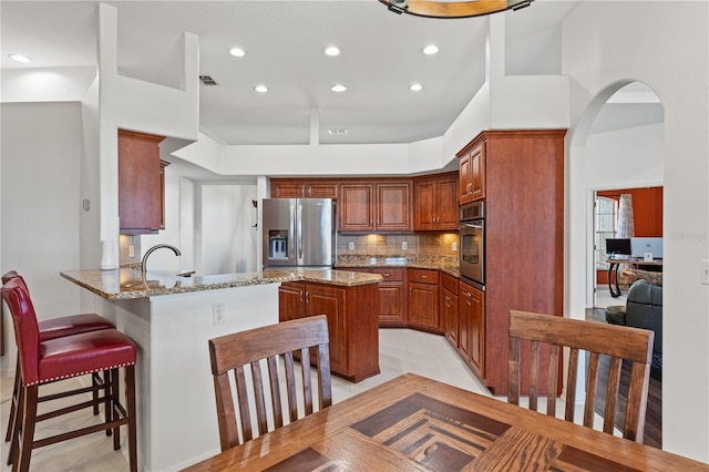 kitchen featuring light stone counters, visible vents, a peninsula, stainless steel appliances, and tasteful backsplash