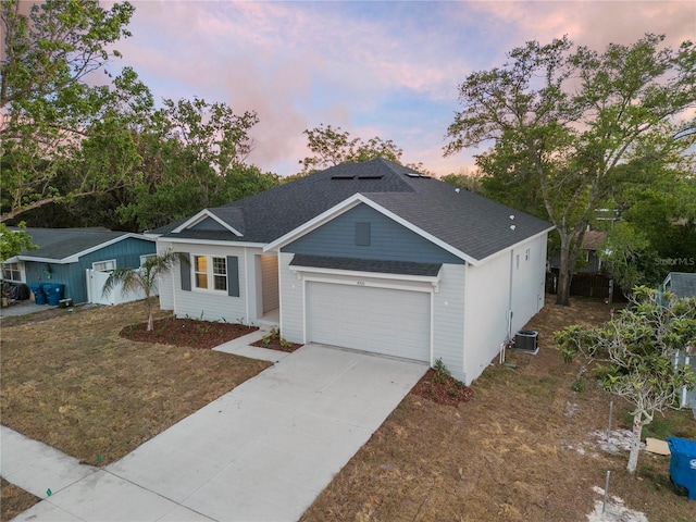 ranch-style home featuring driveway, a shingled roof, a lawn, an attached garage, and central air condition unit