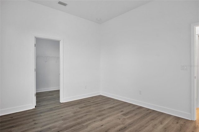 unfurnished bedroom featuring baseboards, visible vents, a walk in closet, and dark wood-type flooring