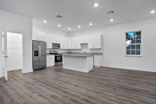 kitchen with stone countertops, visible vents, white cabinets, a kitchen island with sink, and stainless steel appliances