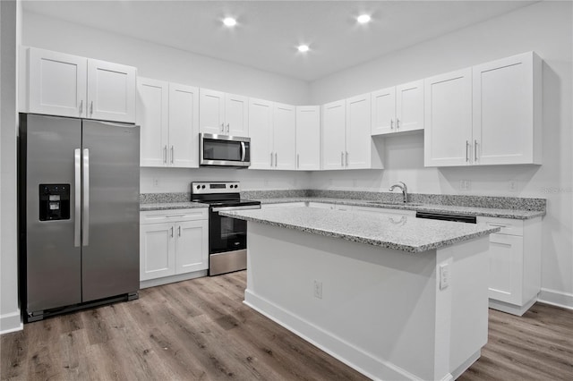 kitchen with white cabinets, light stone countertops, a kitchen island, and stainless steel appliances