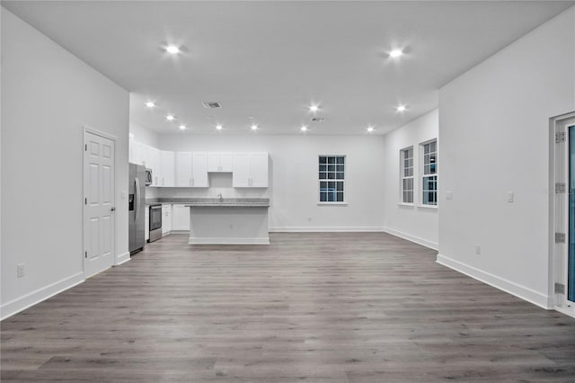 unfurnished living room with baseboards, light wood finished floors, a sink, and recessed lighting