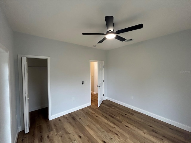 unfurnished bedroom featuring baseboards, visible vents, wood finished floors, a closet, and a walk in closet