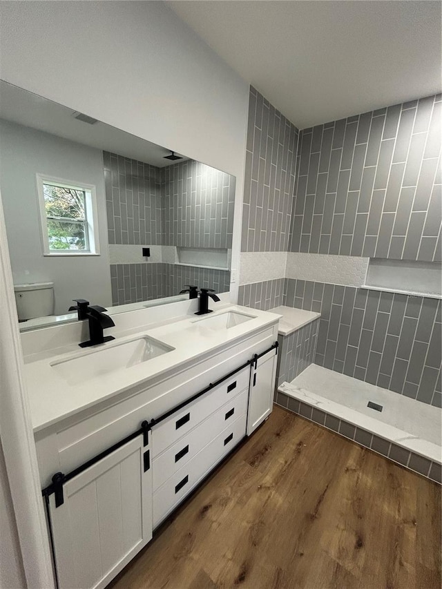 bathroom featuring wood finished floors, a sink, double vanity, and tile walls