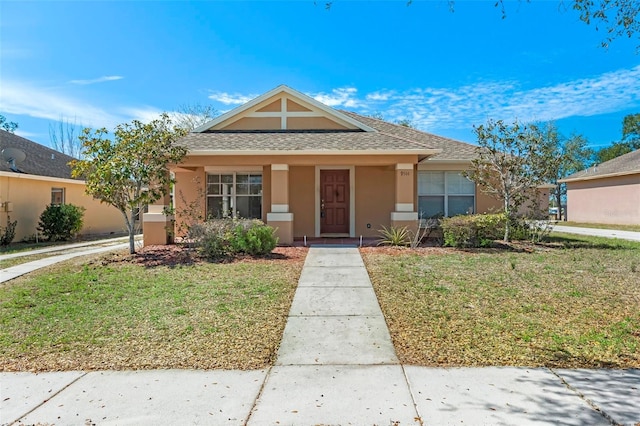 view of front of home with roof with shingles, a front yard, and stucco siding