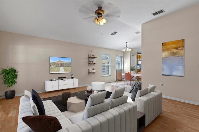 living area featuring visible vents, light wood-style flooring, baseboards, and ceiling fan with notable chandelier