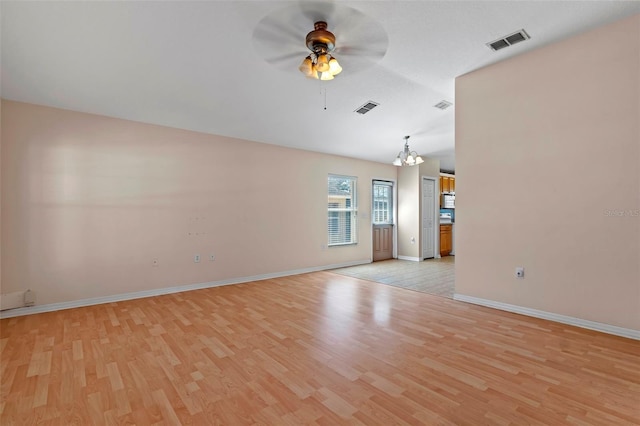 empty room featuring ceiling fan with notable chandelier, light wood-type flooring, visible vents, and baseboards