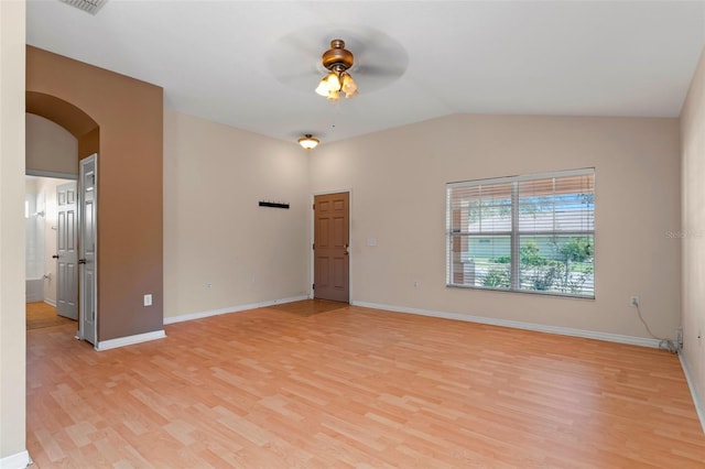 empty room with arched walkways, vaulted ceiling, light wood-style flooring, and baseboards