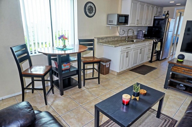 kitchen with light tile patterned floors, decorative backsplash, light stone counters, stainless steel appliances, and a sink