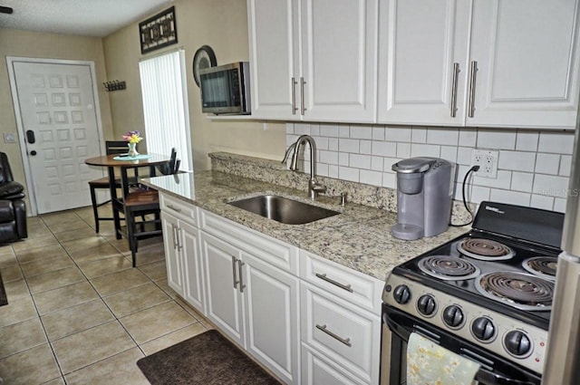 kitchen featuring light stone counters, electric stove, light tile patterned floors, white cabinets, and a sink