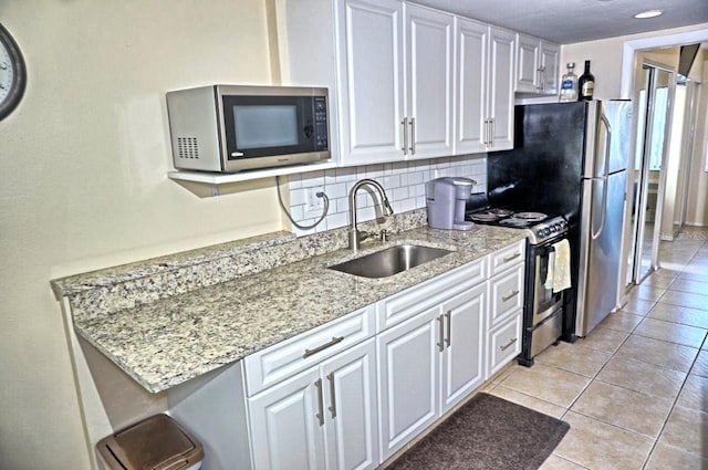 kitchen with light stone counters, stainless steel microwave, electric range, white cabinetry, and a sink