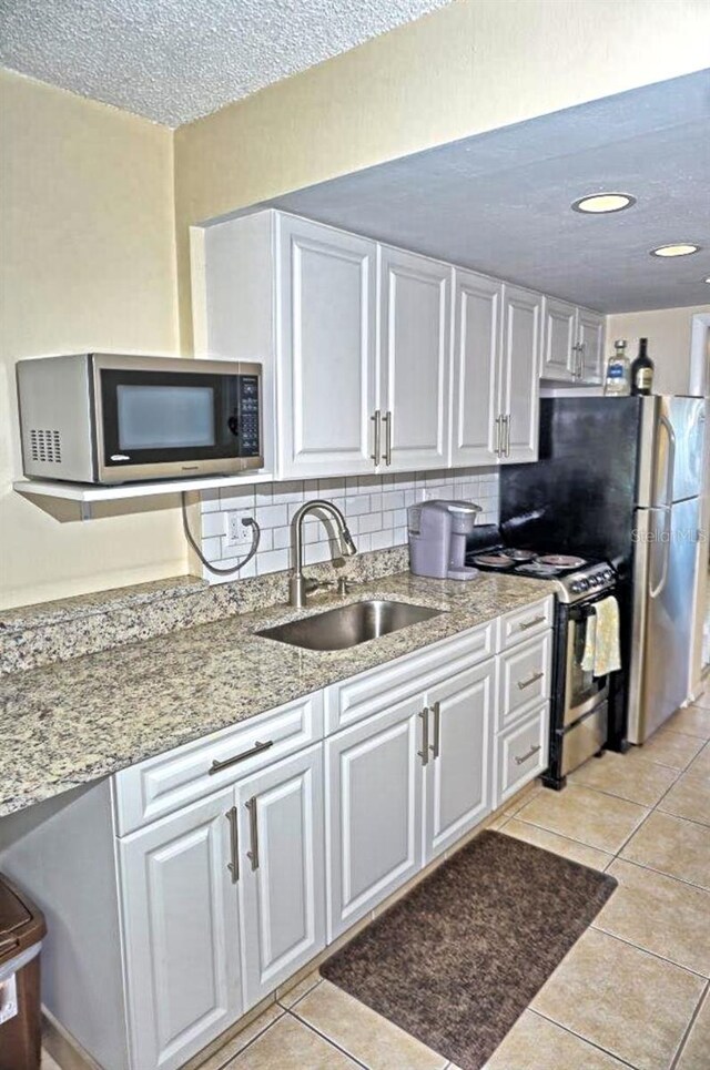 kitchen featuring tasteful backsplash, appliances with stainless steel finishes, light tile patterned flooring, white cabinets, and a sink