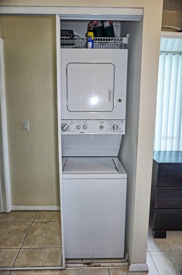 washroom featuring light tile patterned floors, stacked washer and dryer, laundry area, and baseboards