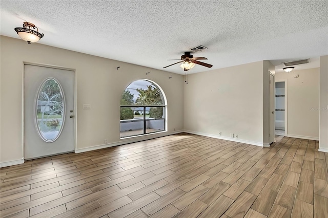 foyer featuring a textured ceiling, visible vents, a ceiling fan, baseboards, and light wood finished floors