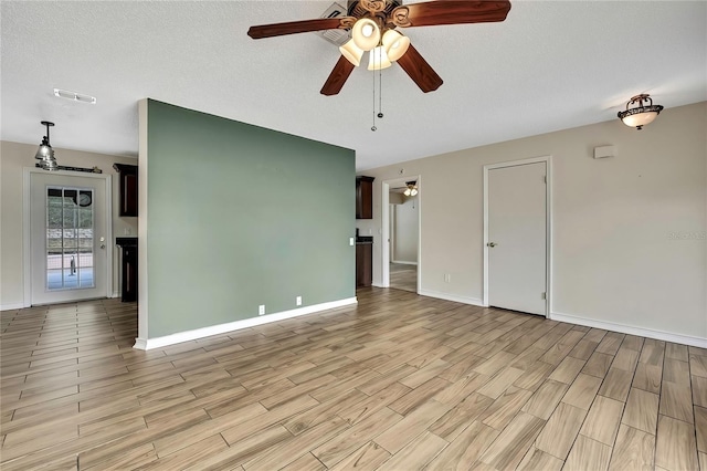 unfurnished room with visible vents, ceiling fan, a textured ceiling, light wood-type flooring, and baseboards