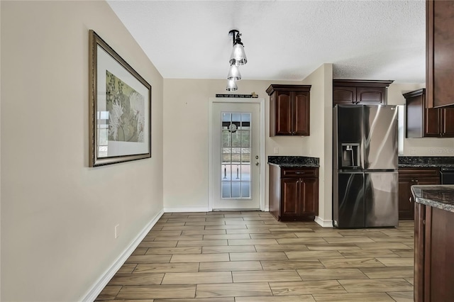 kitchen with wood finish floors, stainless steel fridge with ice dispenser, dark brown cabinets, dark stone counters, and baseboards