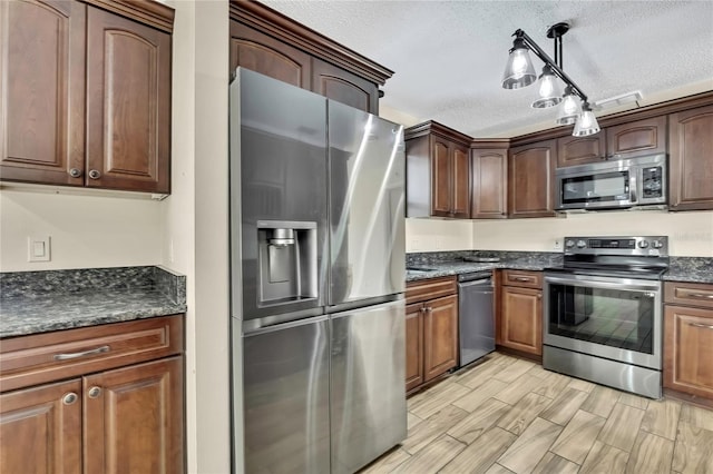 kitchen featuring appliances with stainless steel finishes, dark stone countertops, decorative light fixtures, a textured ceiling, and wood finish floors