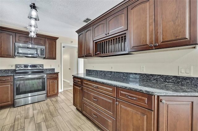 kitchen with a textured ceiling, visible vents, appliances with stainless steel finishes, dark stone countertops, and pendant lighting