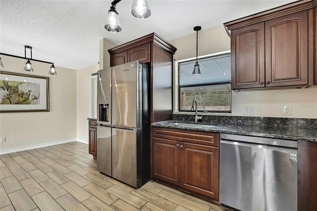 kitchen with dark stone counters, appliances with stainless steel finishes, hanging light fixtures, a textured ceiling, and a sink