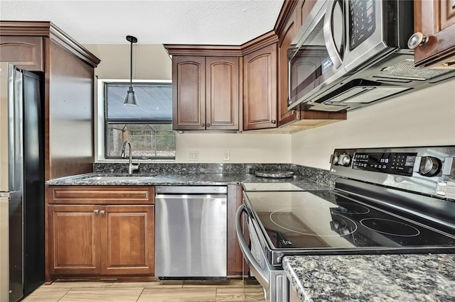 kitchen with dark stone counters, appliances with stainless steel finishes, wood tiled floor, pendant lighting, and a sink