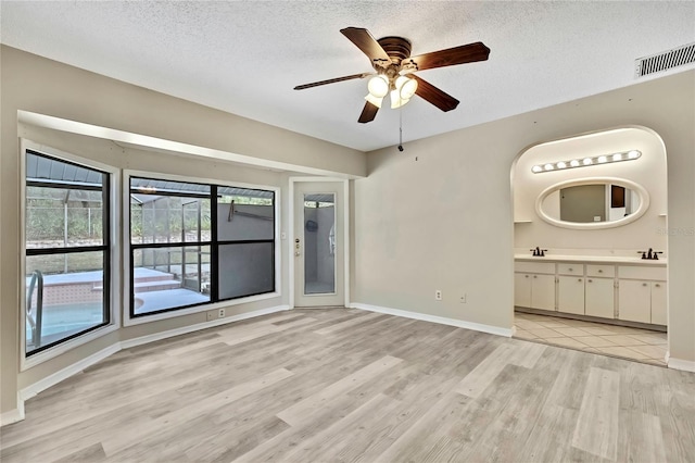 spare room with light wood finished floors, baseboards, visible vents, a textured ceiling, and a sink