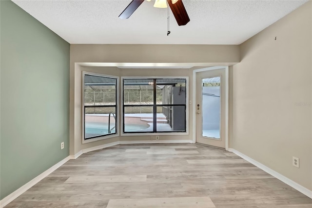 spare room featuring baseboards, light wood-style flooring, and a textured ceiling