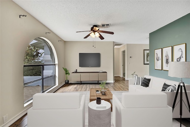 living area featuring light wood-type flooring, a ceiling fan, visible vents, and a textured ceiling