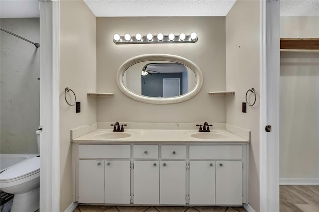 full bath featuring toilet, double vanity, a textured ceiling, and a sink