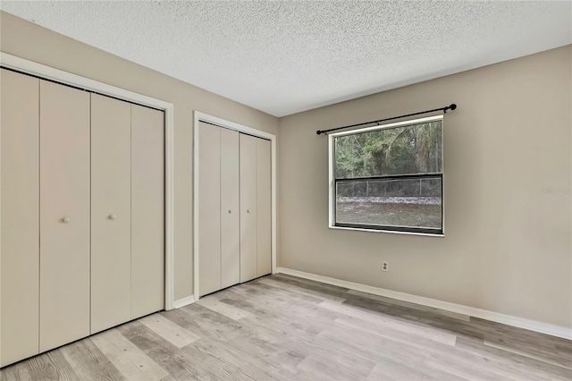 unfurnished bedroom with baseboards, a textured ceiling, light wood finished floors, and two closets