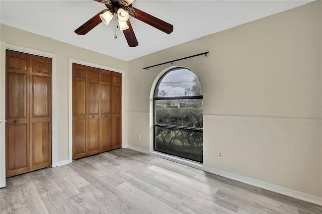 unfurnished bedroom with light wood-style floors, a ceiling fan, baseboards, and two closets