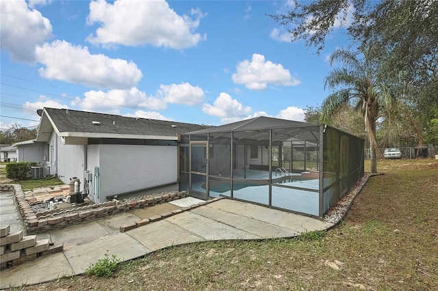 rear view of property with glass enclosure, a patio, central AC, an outdoor pool, and stucco siding