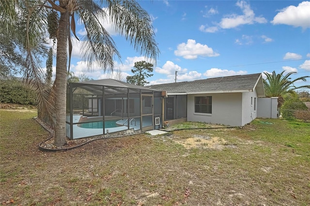 rear view of house featuring a lawn, stucco siding, a lanai, and an outdoor pool