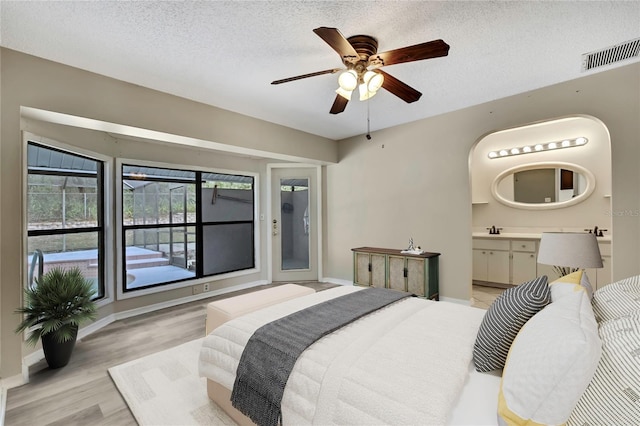 bedroom featuring visible vents, ensuite bathroom, a textured ceiling, light wood-type flooring, and a sink